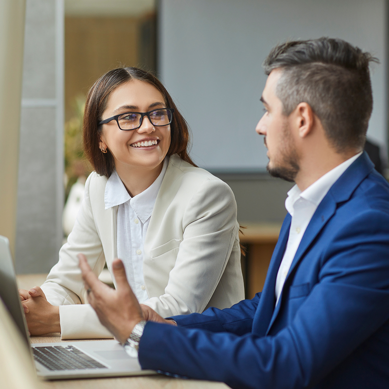 Two young smiling company employees man and woman sitting with laptop having discussion talking